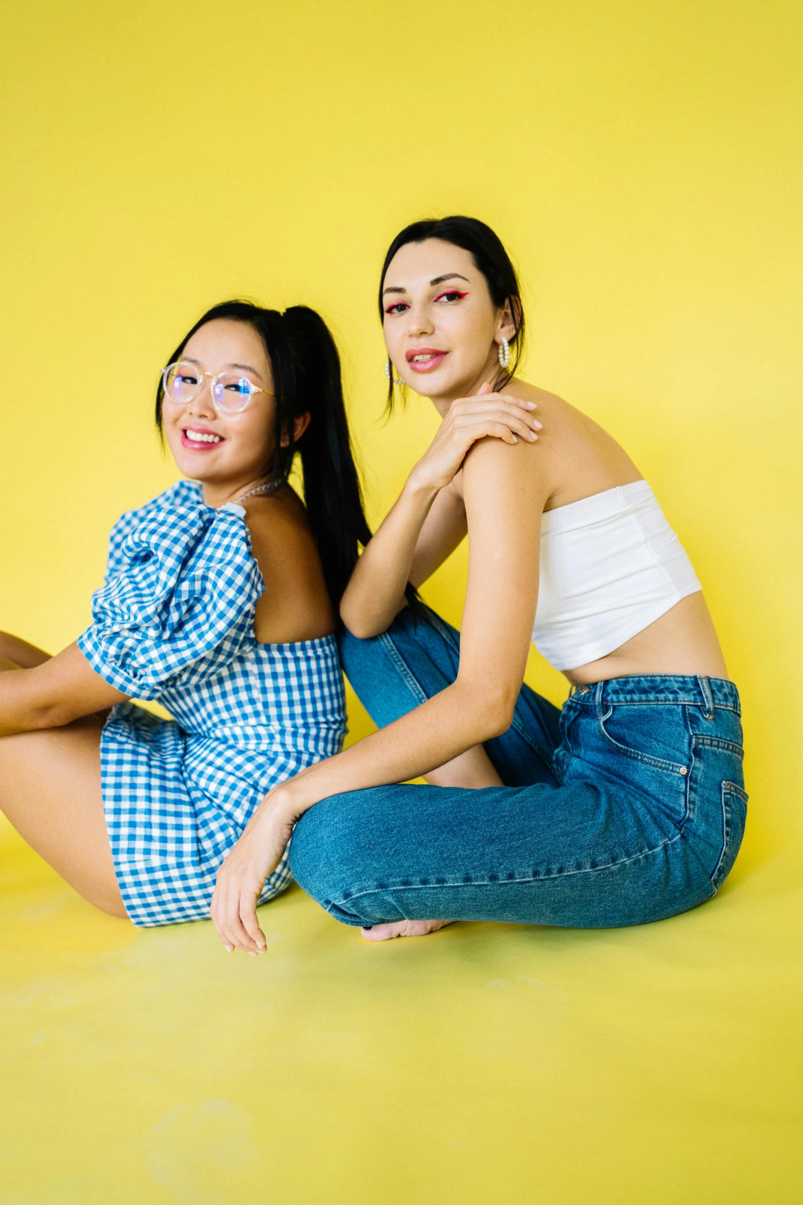 two women sitting next to each other on a yellow background, inspired by Wang Duo, trending on pexels, blue jeans, half asian, modelling, transparent