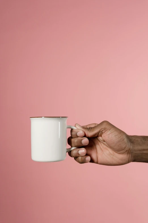 a hand holding a coffee cup against a pink background, by Will Ellis, glossy white metal, handcrafted, hero shot, made of bronze