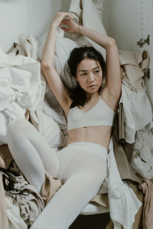 a woman laying on top of a bed next to a pile of clothes, inspired by Ren Hang, pexels contest winner, gutai group, wearing white tights, intense look, maggie cheung, gif