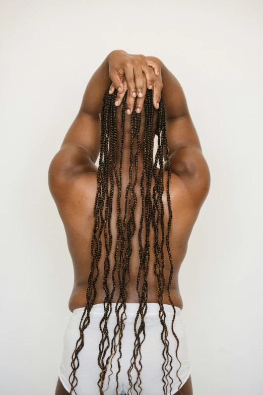 a woman with dreadlocks standing in front of a white wall, with his back turned, complex braided hair, hands straight down, ignant