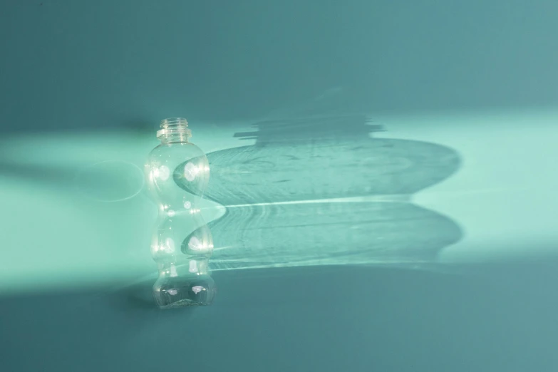 a bottle of water sitting on top of a table, inspired by Bruce Munro, unsplash, light and space, cyan photographic backdrop, light bulbs, rippling reflections, made out of plastic