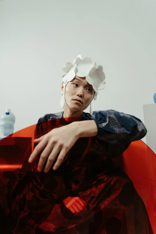 a man sitting in a chair with a paper hat on his head, an album cover, inspired by Gao Cen, an asian woman, issey miyake, eva elfie, flowery