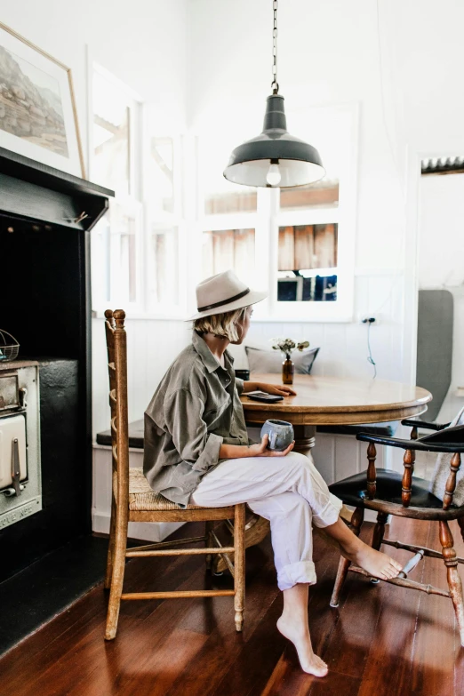 a woman sitting at a table in front of an oven, by Tom Bonson, trending on unsplash, white suit and hat, cottage decor, cafe interior, sydney hanson