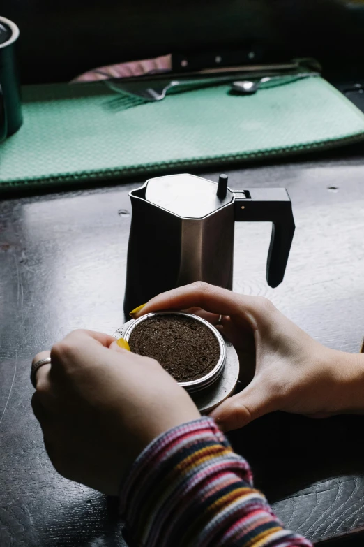 a person sitting at a table with a cup of coffee, stainless steal, blending, pot, no cropping