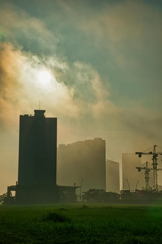 a green field with tall buildings in the background, a matte painting, pexels contest winner, brutalism, industrial fires and smog, sun, construction, smoky