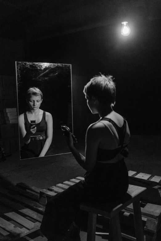 a woman sitting on a stool in front of a mirror, a black and white photo, by Billie Waters, sophia lillis, on a stage, irina nordsol kuzmina, ( ( theatrical ) )