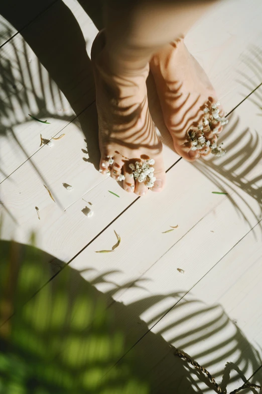 a close up of a person's feet on a tiled floor, by Victorine Foot, unsplash, flowers and foliage, white sand, a wooden, sunlit