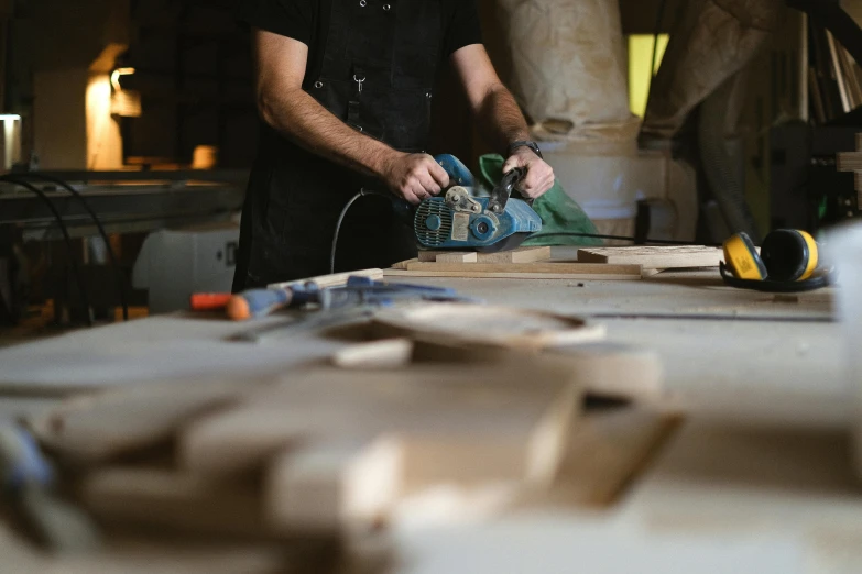 a man sanding a piece of wood on a table, by Matthias Stom, pexels contest winner, john pawson, 🦑 design, : :, holding a chainsaw