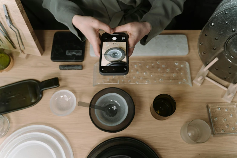 a person sitting at a table with a cell phone, glassware, aperture science, over a dish and over a table, high quality product image”