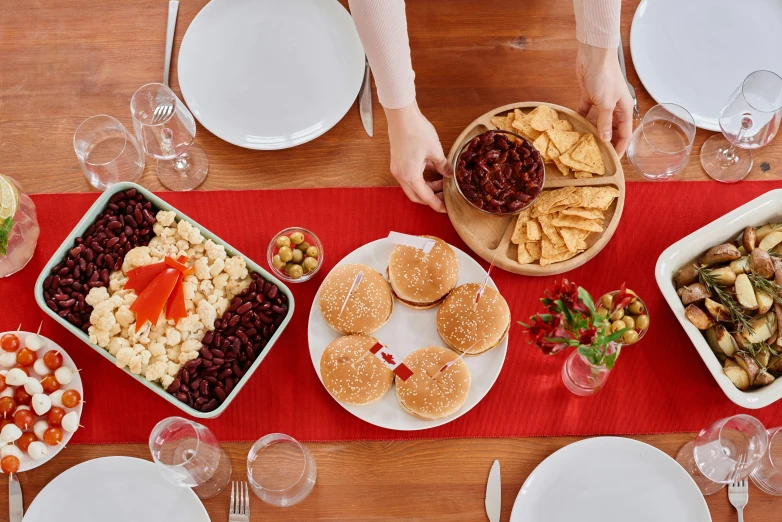 a wooden table topped with plates of food, by Carey Morris, pexels, white and red color scheme, wearing festive clothing, background image, humus