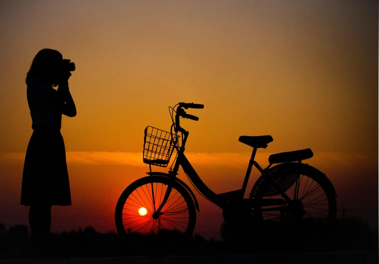 a woman standing next to a bike at sunset, by Hiroshi Honda, pexels contest winner, orange sun set, siluette, fan ho photography, various posed