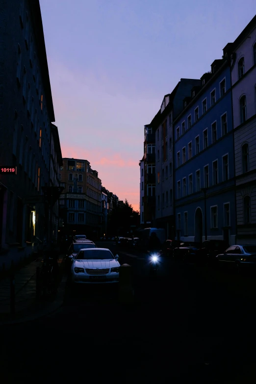 a street filled with lots of traffic next to tall buildings, an album cover, unsplash, berlin secession, late summer evening, barely lit warm violet red light, saint petersburg, calm evening
