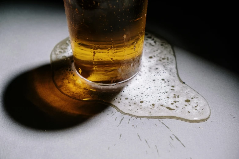 a glass of beer sitting on top of a table, by Adam Marczyński, pexels, puddle of water on the floor, disintegrating, drinking cough syrup, thumbnail