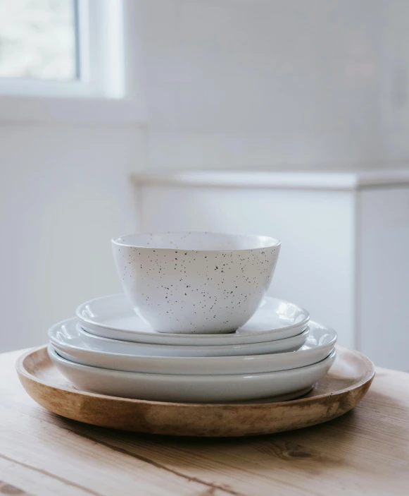 a stack of plates sitting on top of a wooden table, a still life, inspired by Fred Williams, unsplash, white freckles, bowl, set against a white background, on kitchen table