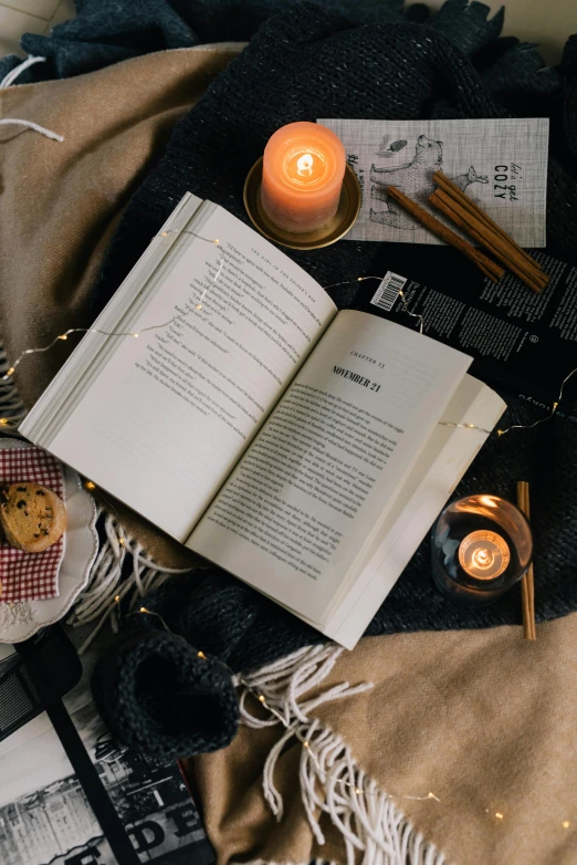 an open book sitting on top of a blanket next to a lit candle, a portrait, pexels contest winner, snacks, flat lay, 15081959 21121991 01012000 4k, books flying around