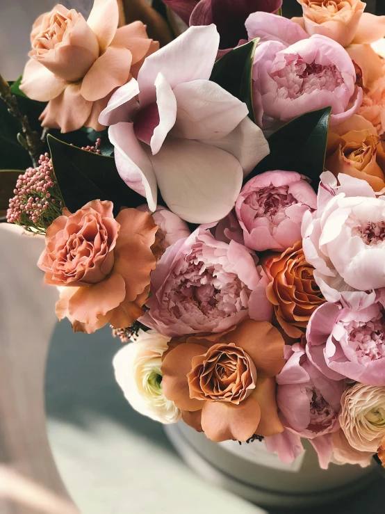 a close up of a vase of flowers on a table, by Leila Faithfull, trending on unsplash, in shades of peach, many peonies, extra detail, abundant detail