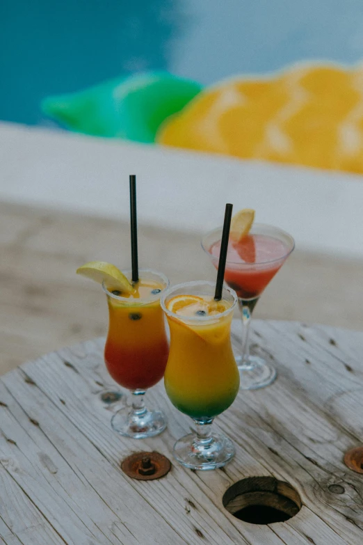 a couple of drinks sitting on top of a wooden table, tropical color scheme, bali, multicoloured, booze