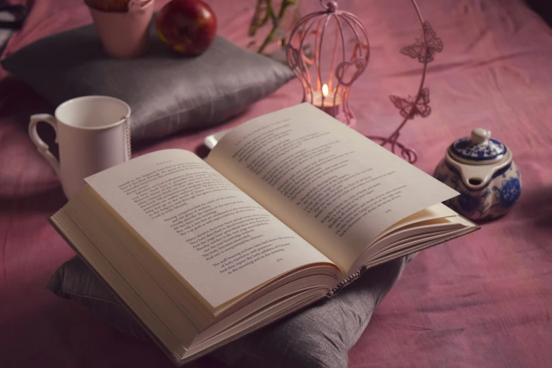 an open book sitting on top of a bed next to a cup of coffee, a still life, by Alice Mason, unsplash, romanticism, soft light 4 k in pink, mary anning, candlelit, striking pose