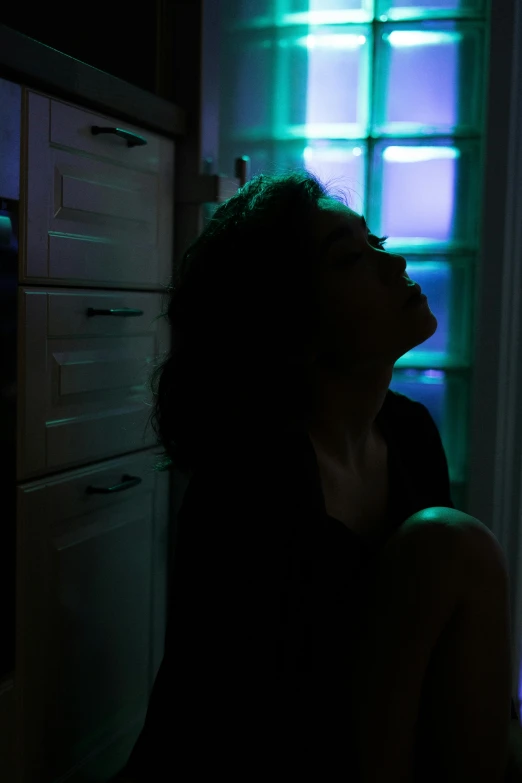 a woman sitting in front of a refrigerator in a dark room, inspired by Elsa Bleda, trending on pexels, bisexual lighting, black silhouette, blue and green light, terrified