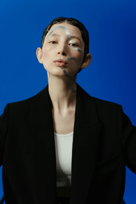 a woman standing in front of a blue background, an album cover, inspired by Gao Cen, neo-dada, emaciated shaved face, woman in black business suit, off - white collection, japanese model