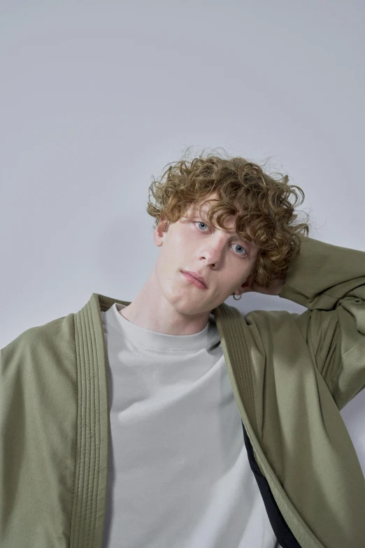 a man with curly hair wearing a green jacket, by Cosmo Alexander, trending on pexels, renaissance, pale skin curly blond hair, with a bob cut, model posing, wearing a grey robe