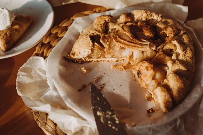 a pie sitting on top of a wooden table, by Emma Andijewska, pexels contest winner, 🎀 🗡 🍓 🧚, parchment paper, traditional corsican, apple