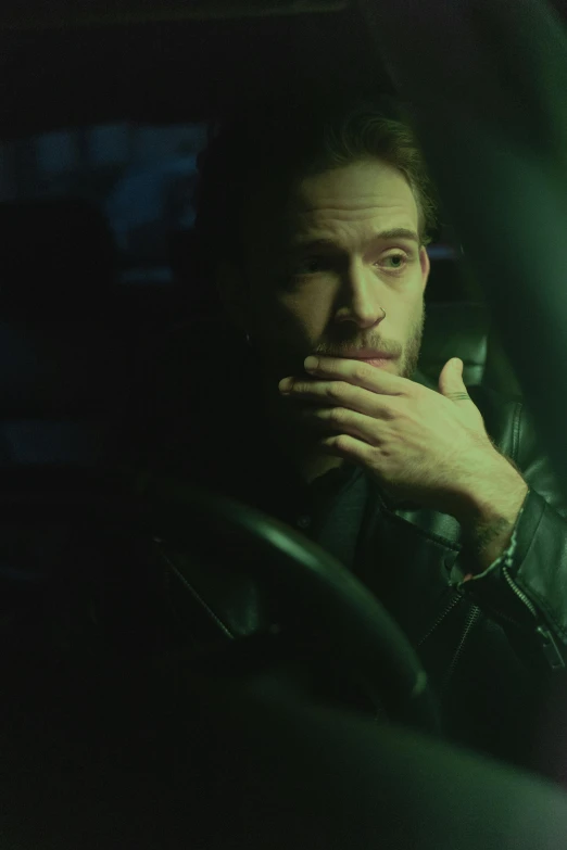 a man sitting in the driver's seat of a car, inspired by Elsa Bleda, very dark with green lights, charlie cox, stillframe, promotional image