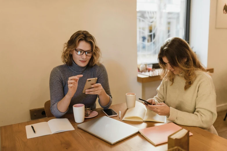 two women sitting at a table looking at their cell phones, trending on pexels, arbeitsrat für kunst, 9 9 designs, studious, avatar image, male and female