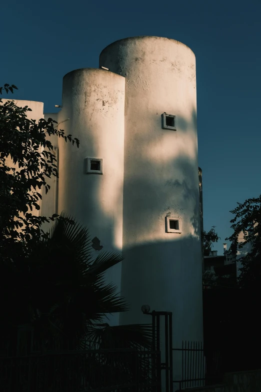 a tall white building sitting on top of a lush green field, inspired by Ricardo Bofill, unsplash, brutalism, warm lighting with cool shadows, marbella, silo, view from the streets