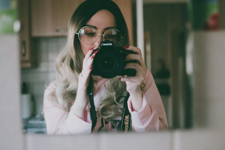 a woman taking a picture of herself in a mirror, a picture, inspired by Elsa Bleda, trending on pexels, photorealism, wearing square glasses, belle delphine, holding a big camera, youtuber