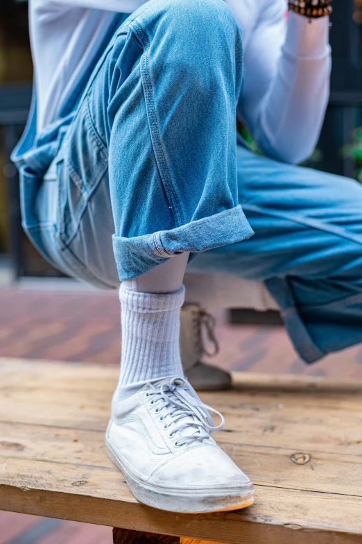 a man sitting on top of a wooden bench, trending on unsplash, hyperrealism, baggy jeans, striped socks, white and pale blue toned, woman in streetwear