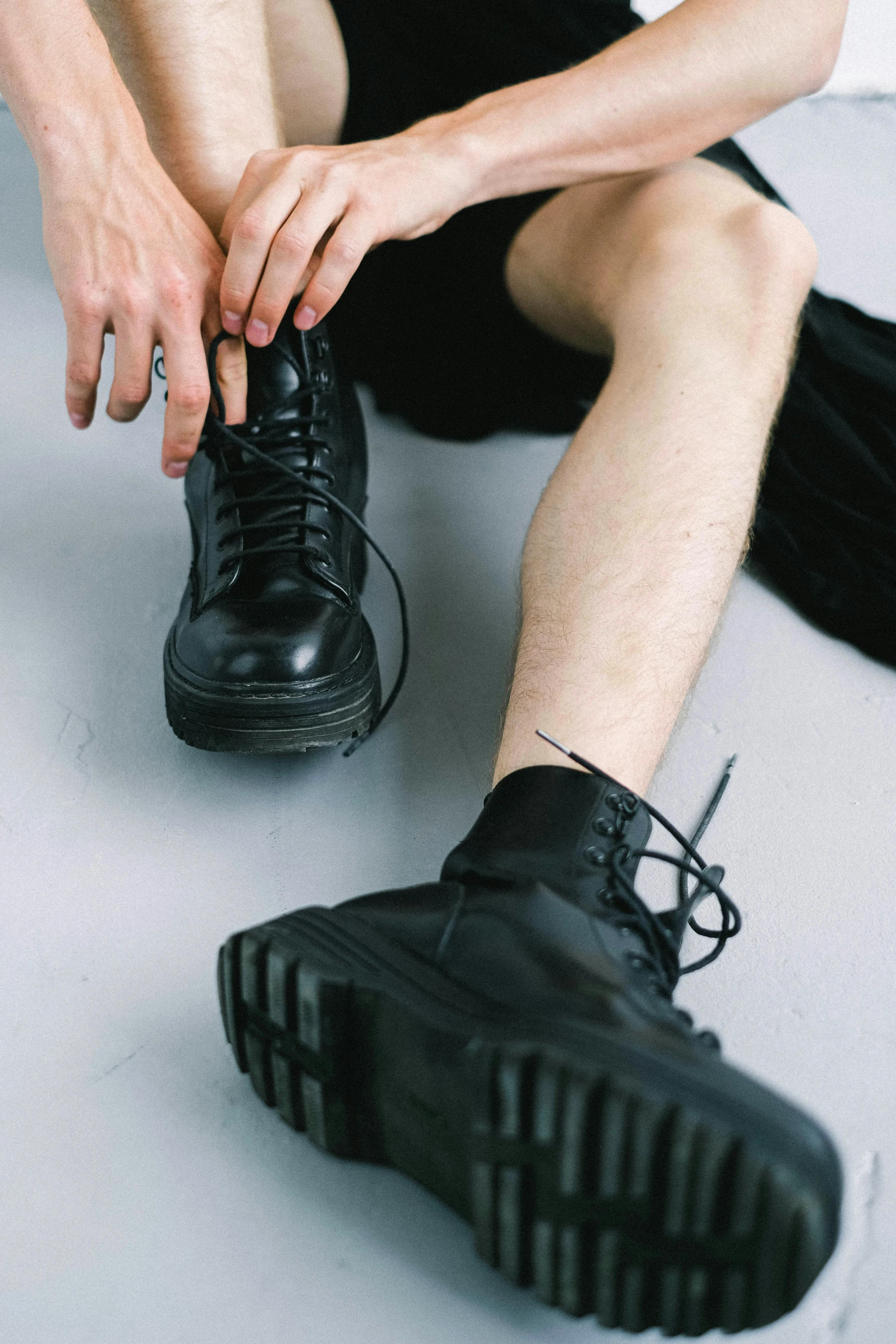 a man sitting on the floor tying up his shoes, inspired by Elsa Bleda, trending on pexels, goth punk clothes, military boots, non binary model, on a pale background