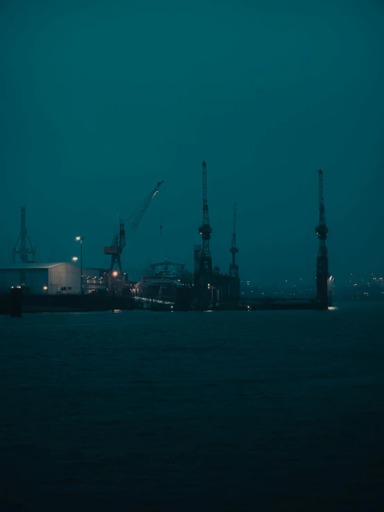 a large body of water with cranes in the background, inspired by Elsa Bleda, pexels contest winner, foggy night, shipyard, petrol aesthetic, movie filmstill