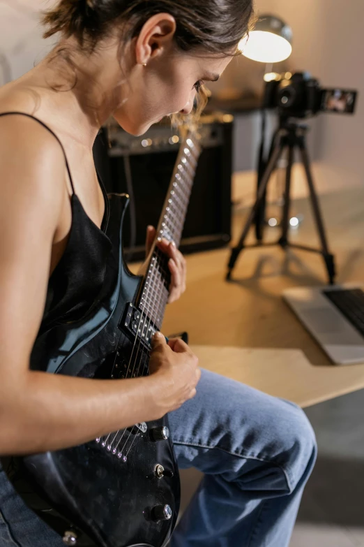 a woman sitting in front of a laptop computer, by Robert Medley, trending on pexels, realism, holding an electric guitar, hyper-detailed. studio lightning, neck zoomed in, bassist