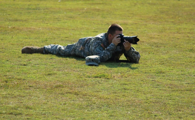 a man that is laying on the ground with a camera, military, rule for thirds, slide show, working out in the field