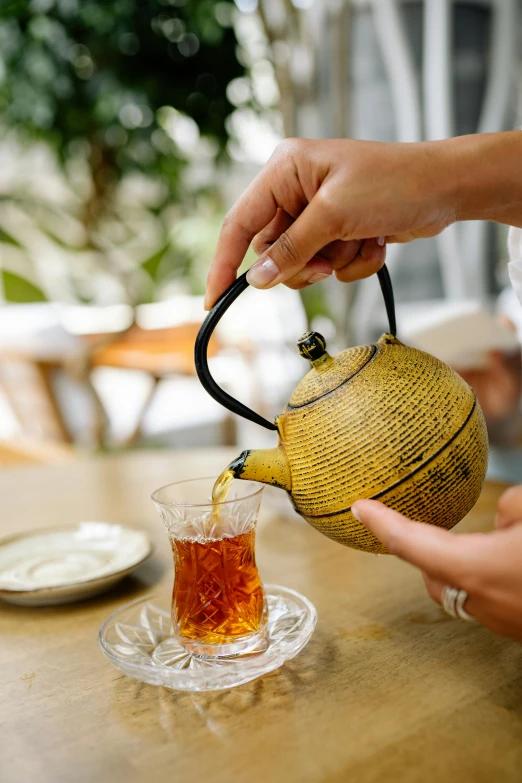 a person pouring tea into a cup on a table, malaysian, teapot : 1, yellow, vintage inspired