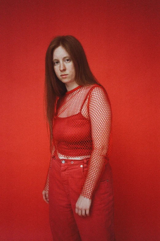 a woman standing in front of a red wall, an album cover, inspired by Julia Pishtar, red shirt, corduroy, red mesh in the facede, on a pale background