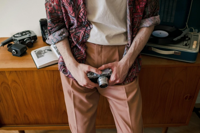 a man standing in front of a record player holding a camera, inspired by Wes Anderson, trending on pexels, brown pants, holster, professional image, holding controller