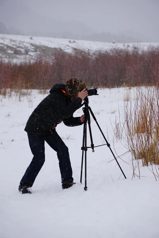 a man that is standing in the snow with a camera, taking a picture