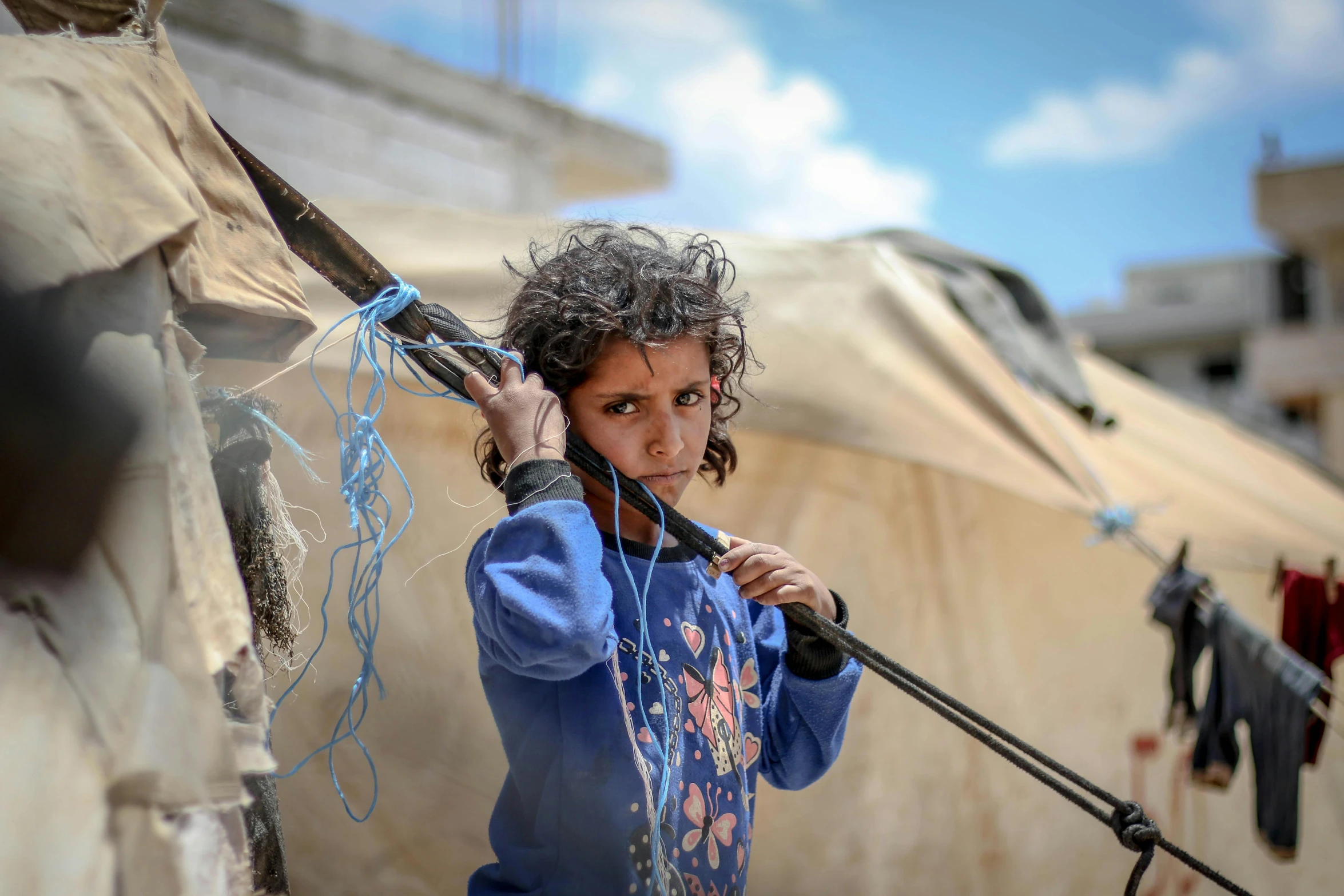 a young girl holding a microphone in front of a tent, by Micha Klein, pexels contest winner, hurufiyya, holding a crossbow, makeshift houses, atef, ripped clothes holding whip