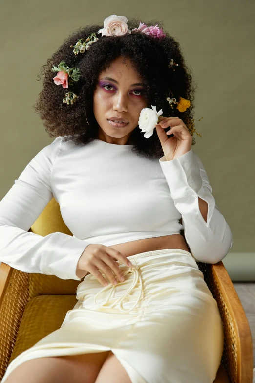 a woman sitting in a chair with a flower in her hair, an album cover, trending on pexels, curly afro, white silky outfit, tinyest midriff ever, shot with sony alpha 1 camera