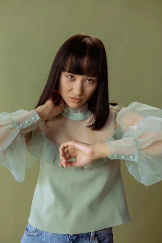 a woman standing in front of a green wall, an album cover, inspired by Miwa Komatsu, trending on pexels, puff sleeves, with index finger, isolate translucent, portrait image