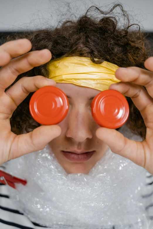 a close up of a person holding two cups in front of their eyes, an album cover, inspired by Julius Klinger, trending on pexels, children playing with pogs, red contact lenses, video game character, david shing
