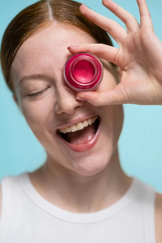 a woman holding a lip bale up to her eye, pexels contest winner, her face in discs, product shoot, cheery, lush