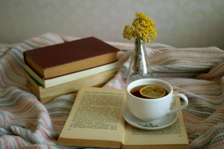 an open book sitting on top of a bed next to a cup of coffee, a still life, pexels contest winner, romanticism, yellow, drinking tea, stack of books on side table, mid-30s