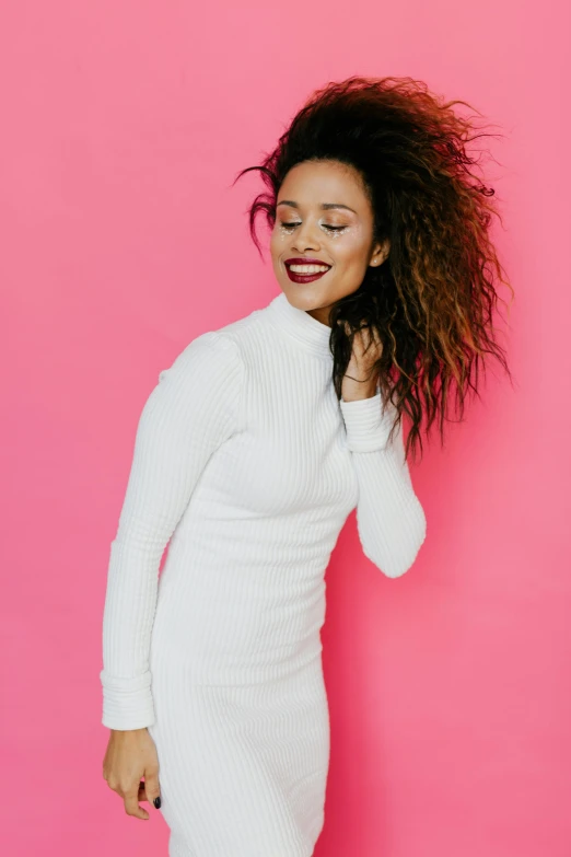 a woman standing in front of a pink wall, an album cover, inspired by Whitney Sherman, trending on pexels, happening, in white turtleneck shirt, mixed race woman, wearing a cute white dress, laughing