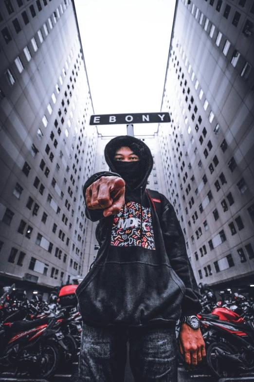 a person standing in front of a bunch of motorcycles, an album cover, inspired by Liam Wong, unsplash contest winner, graffiti, balaclava covering face, stood on top of a sky scraper, pointing at the camera, new york streets