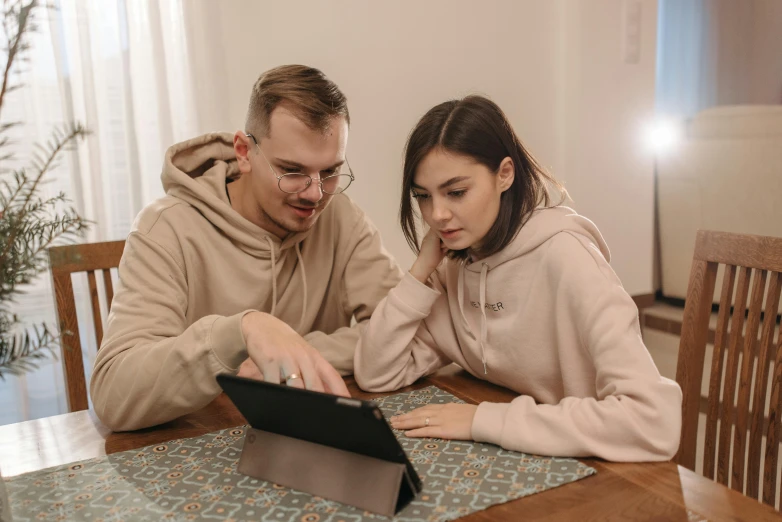 a man and woman sitting at a table looking at a tablet, trending on pexels, realism, beige hoodie, professional photo, decoration, romanian