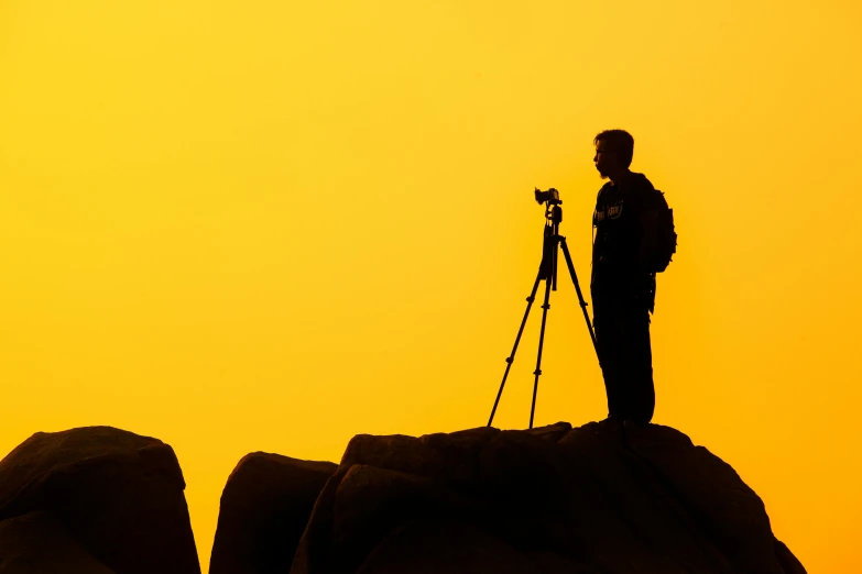 a man standing on top of a rock next to a camera, pexels contest winner, art photography, on a yellow canva, silhouetted, soft light 4k, professional profile picture