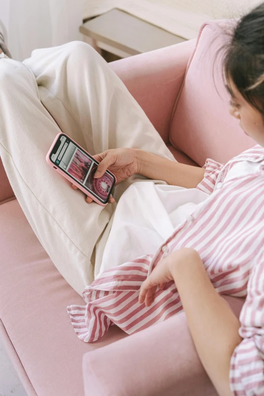 a woman laying on a pink couch holding a cell phone, a cartoon, by Julia Pishtar, trending on pexels, wearing white pajamas, japanese collection product, striped, semi-transparent